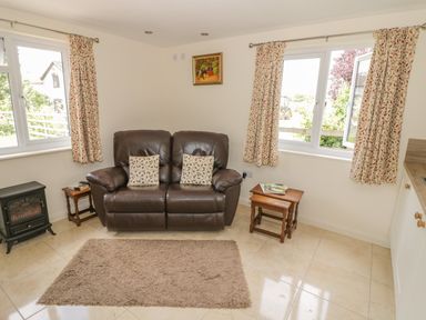 A living room with a brown leather sofa two patterned cushions two wooden tables and a small electric fireplace at Lawn Lodge in Ashleworth