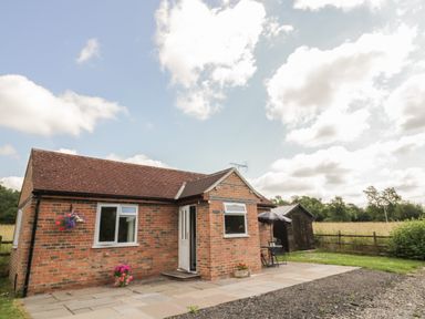 A single-story brick house with a tiled roof and white door in a rural setting with a patio and garden furniture at Lawn Lodge in Ashleworth