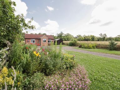 A brick house with a garden full of flowers and a gravel driveway at Lawn Lodge in Ashleworth
