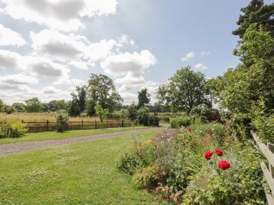 A garden with flowers and a grassy path bordered by a wooden fence at Lawn Lodge in Ashleworth