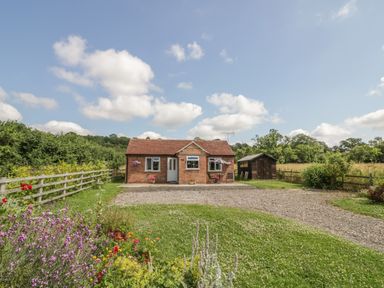 A small brick house with a red roof and gravel driveway with garden and shed at Lawn Lodge in Ashleworth