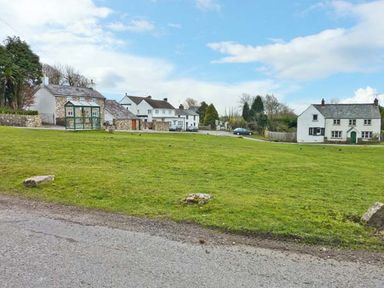 A grassy open area with a greenhouse and several houses in the background at Corner Cottage in Reynoldston near Swansea