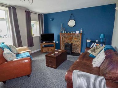 A living room with brown leather sofas a wooden chest coffee table and a TV on a wooden stand at Corner Cottage in Reynoldston near Swansea