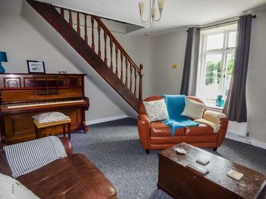 A living room with a piano brown sofas a wooden chest and a window with dark curtains at Corner Cottage Reynoldston near Swansea