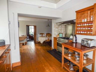 A kitchen with wooden floors wooden furniture a dining table and chairs a stove and kitchen appliances at Corner Cottage in Reynoldston near Swansea