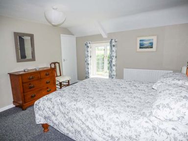 A bedroom with a bed covered in patterned bedding a wooden dresser a chair a window with curtains and a painting on the wall at Corner Cottage in Reynoldston near Swansea