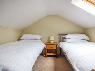 A bedroom with two single beds separated by a wooden nightstand and a lamp at Corner Cottage in Reynoldston near Swansea