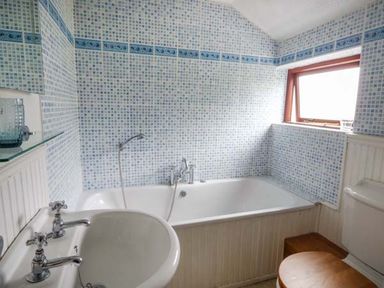 A bathroom with a bathtub sink and toilet with wooden seat at Corner Cottage in Reynoldston near Swansea