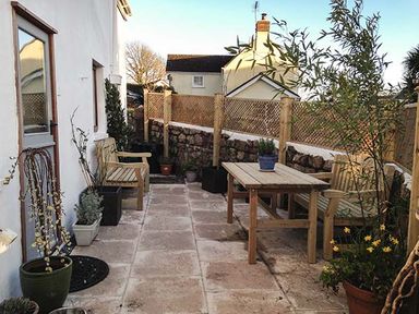 An outdoor patio area with wooden benches and a table surrounded by potted plants and stone and wooden fences at Corner Cottage in Reynoldston near Swansea