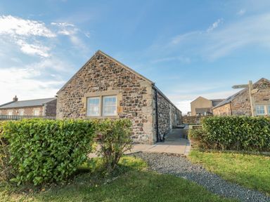 Stone cottages with trimmed bushes and gravel path under blue sky at Long Cart Cottage in Embleton