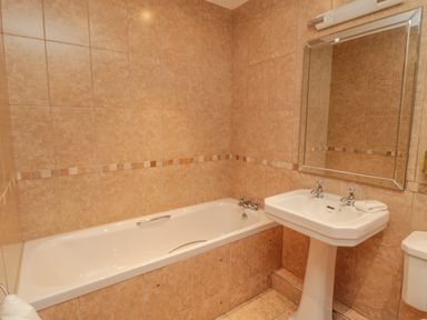 A bathroom with a bathtub a pedestal sink a wall mirror and tiled walls and floor at Long Cart Cottage in Embleton