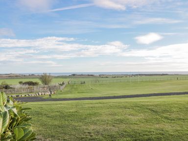 A grassy field with rugby posts and a fence with a view of the sea at Long Cart Cottage in Embleton