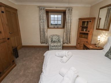 A bedroom with a bed, chair, table, and wardrobe at Long Cart Cottage in Embleton