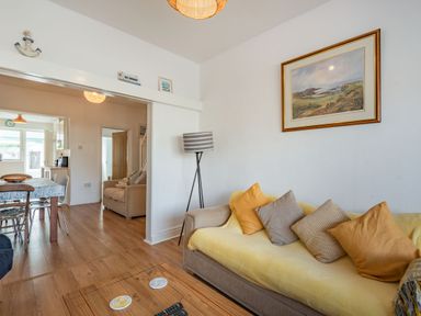 A living room with a sofa and cushions adjacent to a dining area with a table and chairs at 2 Tregof Terrace in Cemaes Bay