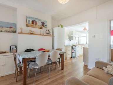 A dining area with a wooden table and six chairs next to a kitchen with white cabinets and appliances at 2 Tregof Terrace in Cemaes Bay