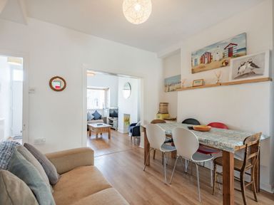 A dining area with a wooden table and mixed chairs next to a sitting area with sofas and a coffee table at 2 Tregof Terrace in Cemaes Bay