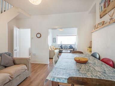 A dining area with a covered table and chairs next to a living room with sofas and cushions at 2 Tregof Terrace in Cemaes Bay