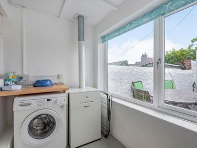 A utility room with a washing machine and heating unit next to a window overlooking a patio at 2 Tregof Terrace in Cemaes Bay