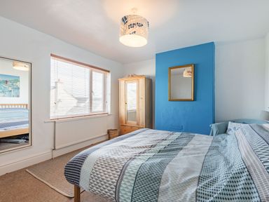 A bedroom with a bed a wooden wardrobe a mirror and a window at 2 Tregof Terrace in Cemaes Bay