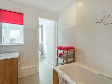 A bathroom with a bathtub a towel rack with folded towels a sink cabinet and a window with a red blind at 2 Tregof Terrace in Cemaes Bay