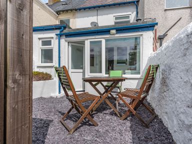 An outdoor patio with a wooden table and three wooden chairs with green cushions at 2 Tregof Terrace in Cemaes Bay
