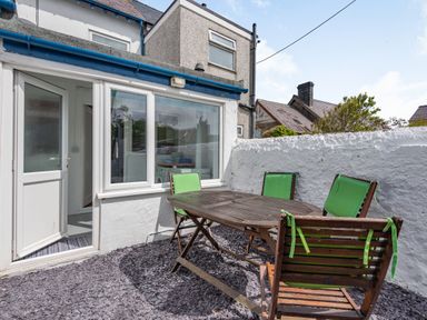 An outdoor patio with a wooden table and four chairs with green cushions at 2 Tregof Terrace in Cemaes Bay