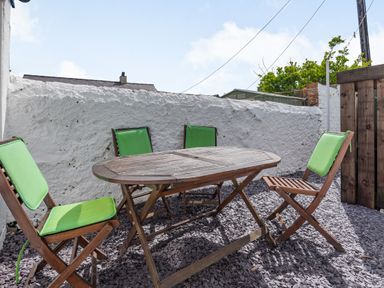 An outdoor patio area with a wooden table and four wooden chairs with green cushions at 2 Tregof Terrace in Cemaes Bay