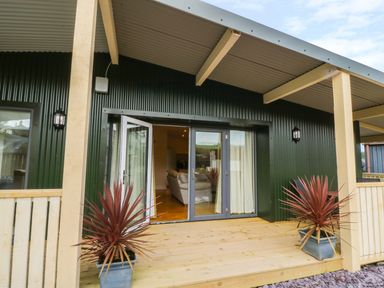 A wooden porch with potted plants in front of glass doors leading to a living room at Y Felin - Moana in Borth near Aberystwyth