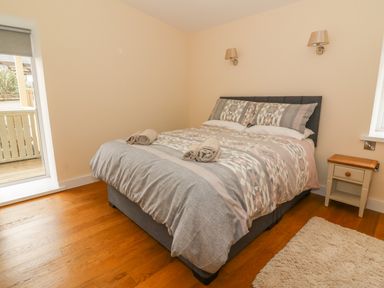 A bedroom with a double bed with patterned bedding and two rolled towels on it a bedside table a window and a door leading outside at Y Felin - Moana in Borth near Aberystwyth
