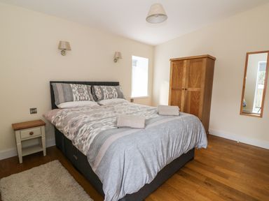 A bedroom with a double bed, bedside table, wooden wardrobe, mirror on the wall, and wooden floor at Y Felin - Moana in Borth near Aberystwyth