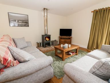 A living room with two sofas a coffee table a wood stove and a television at Y Felin - Moana in Borth near Aberystwyth