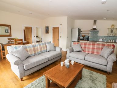 A living room with two sofas and a wooden coffee table next to a dining table and kitchen at Y Felin - Moana in Borth near Aberystwyth