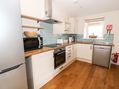 A kitchen with white cabinets wooden countertops a microwave oven toaster kettle dishwasher and a window at Y Felin - Moana in Borth near Aberystwyth