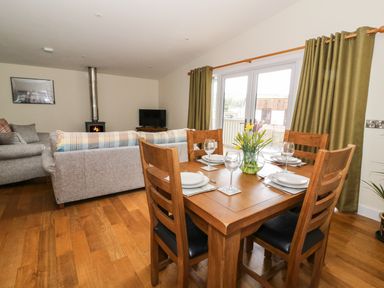 A dining area with wooden table and chairs set for four next to a living room with sofas a wood stove and a television at Y Felin - Moana in Borth near Aberystwyth