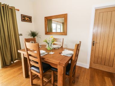 A dining room with a wooden table set for four with plates glasses and flowers at Y Felin - Moana in Borth near Aberystwyth