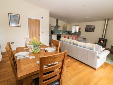 A dining table with four place settings and flowers next to a living area with sofas and a wood stove at Y Felin - Moana in Borth near Aberystwyth