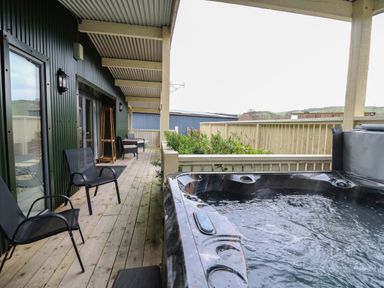 An outdoor covered wooden deck with black chairs a small table and a hot tub at Y Felin - Moana in Borth near Aberystwyth