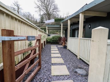 A pathway with square stepping stones leading to a covered porch at a house with a wooden gate labeled Moana at Y Felin - Moana in Borth near Aberystwyth