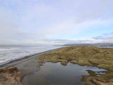 A coastal scene with grassy sand dunes a small pond a pebble beach and the ocean at Y Felin - Moana in Borth near Aberystwyth