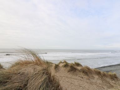 A sandy beach with grass covered dunes and ocean waves at Y Felin - Moana in Borth near Aberystwyth