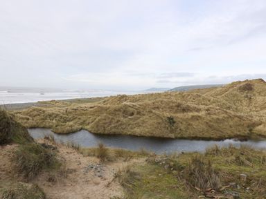 A coastal landscape with grassy sand dunes and a small water body near the sea at Y Felin - Moana in Borth near Aberystwyth
