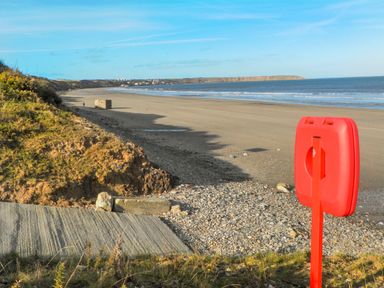 A sandy beach with a red life buoy stand and cliffs in the distance at White Rose Apartment in Filey