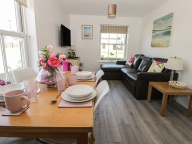 A dining table set with plates and cups and a vase of flowers next to a living room with a leather sofa and a side table with a lamp at White Rose Apartment in Filey