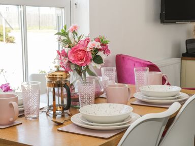A dining table set with plates mugs glasses and a flower vase at White Rose Apartment in Filey
