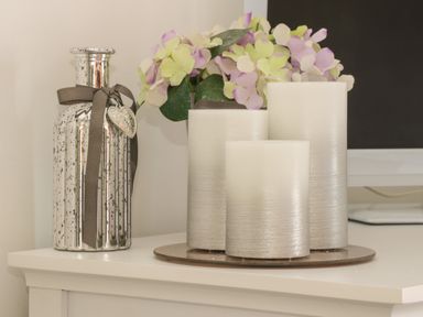 Three pillar candles and a silver decorative bottle with a ribbon on a white surface at White Rose Apartment in Filey