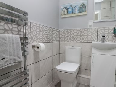 A bathroom with a toilet a sink a towel rack with towel and patterned wall tiles at White Rose Apartment in Filey