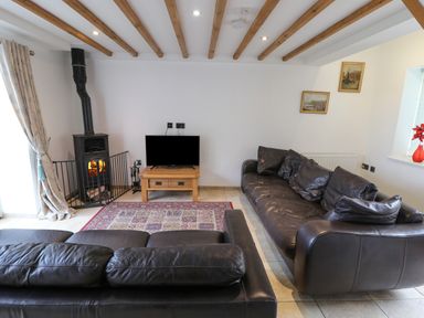A living room with two black leather sofas a wood burning stove a wooden coffee table with a television and framed pictures on the wall at Kingfisher in Whitby