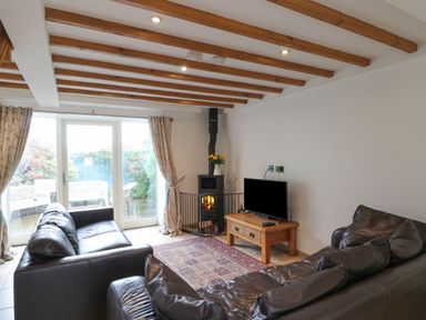 A living room with two brown leather sofas a wooden coffee table with a TV a fireplace with flowers on top and glass doors leading outside at Kingfisher in Whitby