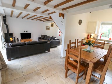 An open plan living room and kitchen with wooden dining table chairs leather sofas wood burning stove and tiled floor at Kingfisher Whitby