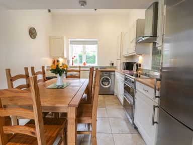 A kitchen with wooden dining table and chairs washing machine stove and refrigerator at Kingfisher in Whitby
